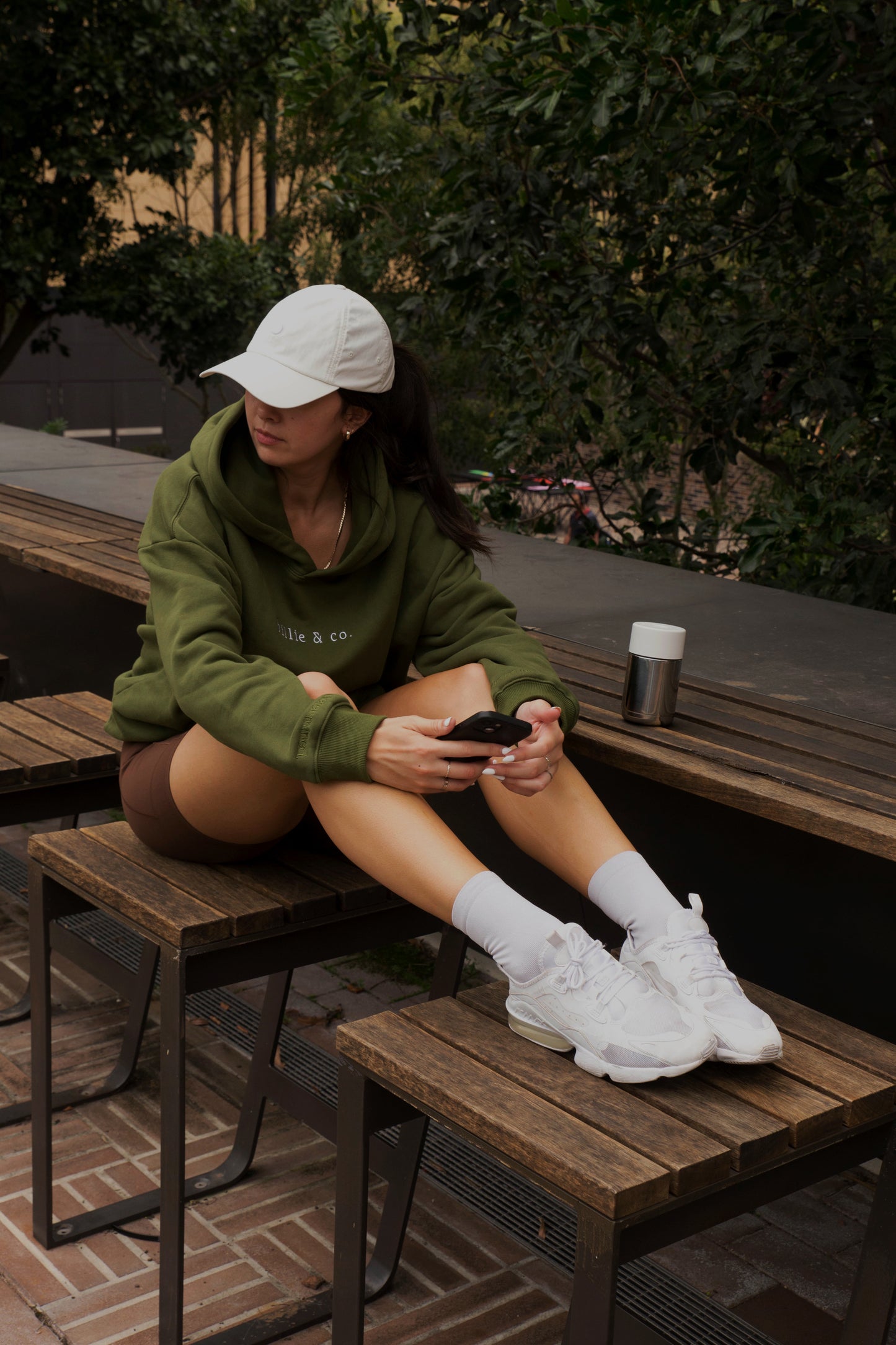 Model wearing an olive green “billie & co.” hoodie with white embroidered text on the chest, while in active wear.