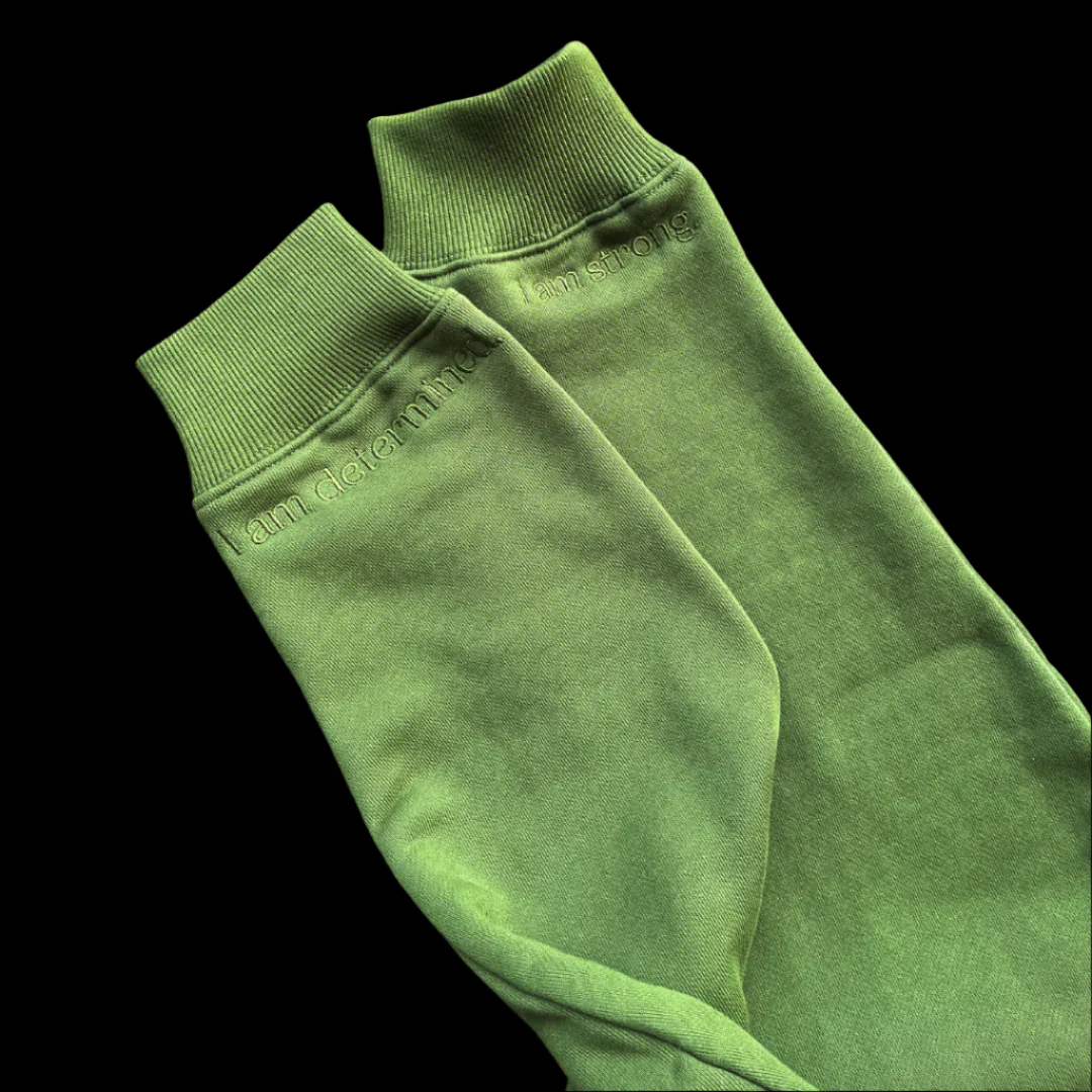 Close-up of two billie & co. olive hoodie sleeves with ribbed cuffs, embroidered with the affirmations “I am determined.” and “I am strong.” in tonal thread.